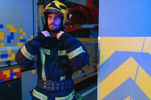 fireman in protective uniform standing near fire engine on station photo