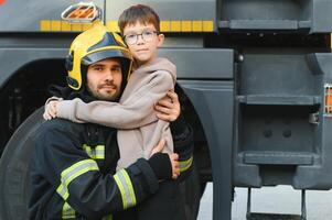 A firefighter take a little child boy to save him. Fire engine car on background photo