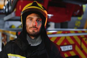 retrato de un bombero en un protector traje y un protector casco en pie por un fuego motor después trabajando en un fuego. de cerca imagen foto