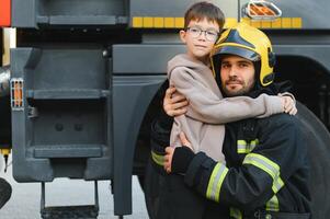 A firefighter take a little child boy to save him. Fire engine car on background photo