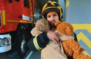 A firefighter take a little child boy to save him. Fire engine car on background photo