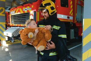 A firefighter take a little child boy to save him. Fire engine car on background photo