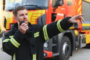 Firefighter in uniform using portable radio set near fire truck outdoors photo