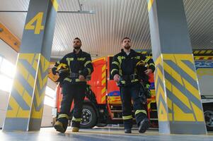 Group of firefighters at the emergency vehicle in the fire station photo