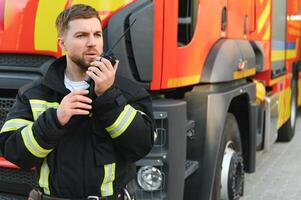 Firefighter in uniform using portable radio set near fire truck outdoors photo