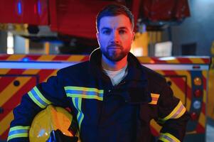 fireman in protective uniform standing near fire engine on station photo