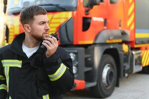 Firefighter in uniform using portable radio set near fire truck outdoors photo