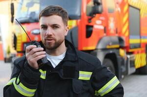 Firefighter in uniform using portable radio set near fire truck outdoors photo