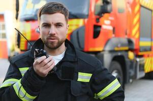 Firefighter in uniform using portable radio set near fire truck outdoors photo