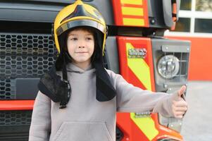 A boy wearing a fireman's helmet near a fire truck. photo