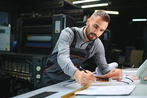 Print house worker controlling printing process quality and checking colors with magnifying glass photo