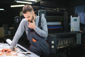 Print house worker controlling printing process quality and checking colors with magnifying glass photo