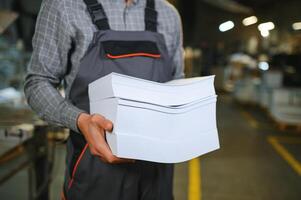 Close up of man putting stack of paper in printing machine at publishing shop, copy space photo