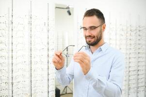 joven hombre elegir gafas a óptico tienda foto