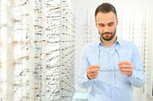 Healthcare, Eyesight And Vision Concept. Happy man choosing glasses at optics store, selective focus photo