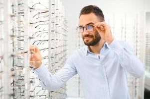 cuidado de la salud, vista y visión concepto. contento hombre elegir lentes a óptica almacenar, selectivo atención foto