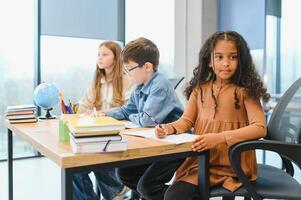 Focused multiracial students kids writing down data into notebook while sitting at table photo