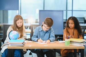 enfocado multirracial estudiantes niños escritura abajo datos dentro cuaderno mientras sentado a mesa foto
