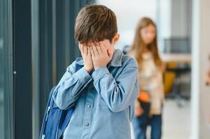 School friends bullying a sad boy in corridor at school photo