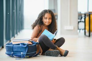 Girl smiling. Beautiful african american schoolgirl smiling while sitting near window and reading book photo