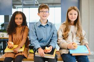 multirracial Niños de escuela teniendo almuerzo a el escritorio durante un descanso en colegio foto