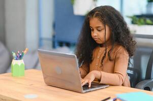 African american girl sitting at table, using laptop for online lesson photo