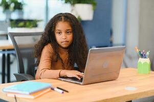 African american girl sitting at table, using laptop for online lesson photo