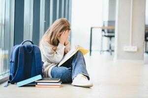 Side view of sad school girl sitting on floor at corridor and hiding face by hands and crying. photo