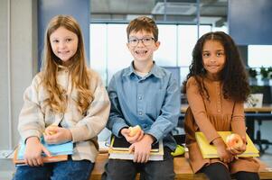 multirracial Niños de escuela teniendo almuerzo a el escritorio durante un descanso en colegio foto