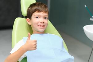 Little boy sits on dentist's chair in good mood after dental procedures. Young patient with healthy teeth photo