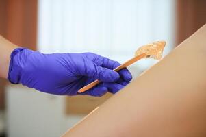 Woman having hair removal procedure on leg with sugaring paste in salon photo