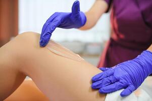 Woman having hair removal procedure on leg with sugaring paste in salon photo