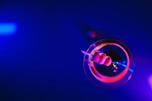 Martini glass and olives on a black background with neon lights photo