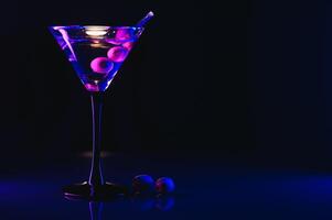martini vaso y aceitunas en un negro antecedentes con neón luces foto