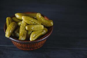 Pickled gherkins or cucumbers in bowl on wooden rustic table from above. photo