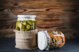 Jars of pickled vegetables on rustic wooden background photo