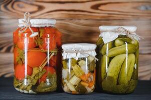 Canned cucumbers and tomatoes with craft lids on a wooden background. Cucumbers and tomatoes with place for text. Stocks of canned food. Harvest, stocks for the winter. photo