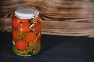 Homemade pickled tomatoes in glass jars on rustic wooden background. Fermented tomatoes in transparent glass. Homemade canned tomatoes. photo