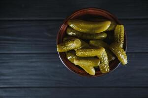 Pickled gherkins or cucumbers in bowl on wooden rustic table from above. photo