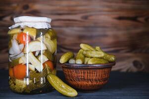 Glass jars with pickled cucumbers pickles, pickled tomatoes and cabbage. Jars of various pickled vegetables. Canned food in a rustic composition. photo