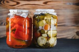 Jars of pickled vegetables on rustic wooden background photo