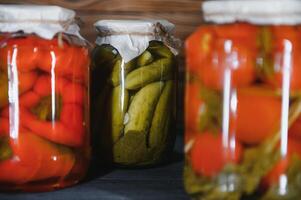 Canned cucumbers and tomatoes with craft lids on a wooden background. Cucumbers and tomatoes with place for text. Stocks of canned food. Harvest, stocks for the winter. photo