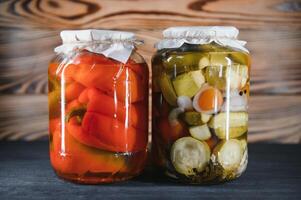 Canned cucumbers and tomatoes with craft lids on a wooden background. Cucumbers and tomatoes with place for text. Stocks of canned food. Harvest, stocks for the winter. photo