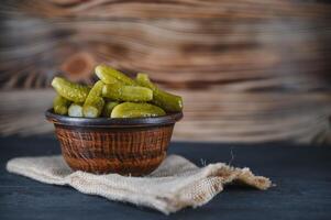 Pickled gherkins or cucumbers in bowl on wooden rustic table from above. photo