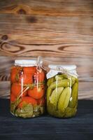 Canned cucumbers and tomatoes with craft lids on a wooden background. Cucumbers and tomatoes with place for text. Stocks of canned food. Harvest, stocks for the winter. photo