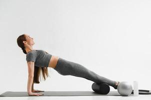 Fit young brunette pilates instructor showing different exercises on a white background a mat. photo