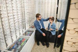 Dad and son choose new stylish glasses in an optical store. Vision care concept photo