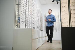 Shot of a handsome bearded man trying on new glasses at the eyewear store.Man buying glasses.Health, eyesight, vision, fashion, shopping photo