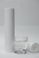 A glass of drink water and filter cartridges at white background photo