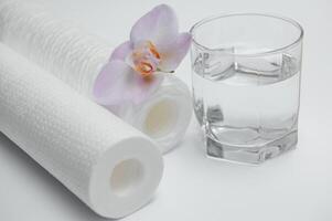 A glass of drink water and filter cartridges at white background photo